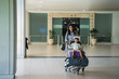 © Odua Images - Asian mom looks at the camera while walking pushing the trolley towards the airport waiting room