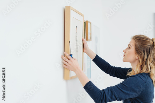 Fotografía Young woman hanging a picture on a wall