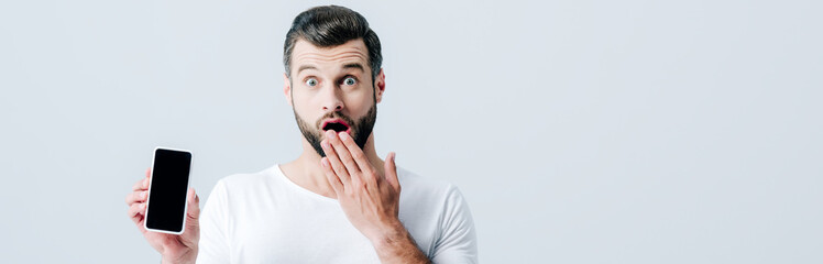 panoramic shot of shocked man showing smartphone with blank screen isolated on grey