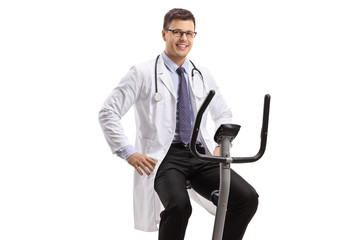 Wall Mural - Young male doctor on a stationary bike looking at the camera and smiling