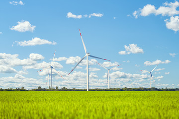 Wind power plant in the green field against cloudy sky