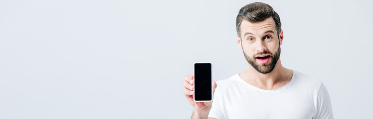 panoramic shot of shocked man showing smartphone with blank screen isolated on grey