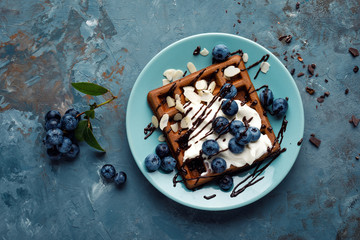 Sticker - Chocolate belgian waffles with ice cream and fresh blueberry on blue background, top view