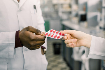 Wall Mural - Male And Female Pharmacists or doctors In Pharmacy. Welcome in drugstore. Cropped image of hands of pharmacists or doctors holding blister of red capsules