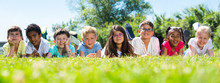 Happy Children Resting On Grass And Smiling Together In Park