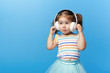 Happy smiling child enjoys listens to music in headphones over colorful bleu background. Vivid and fun emotions, happy child with pleasure listens to songs in wireless headphones