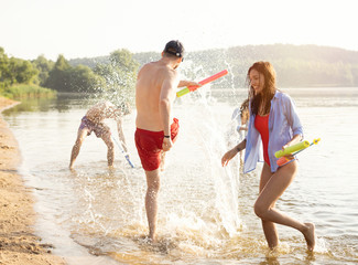 Happy people with water guns have fun on the beach