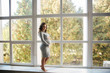 © Aleksandr - Pregnant woman in a beautiful gray dress standing near the window and stroking her tummy
