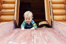 Cute Adorable Caucasian Toddler Boy Having Fun Sliding Down Wooden Slide At Eco-friendly Natural Playground At Backyard In Autumn. Playful Funny Child Portrait Enjoying Outdoor Sport Acitivities