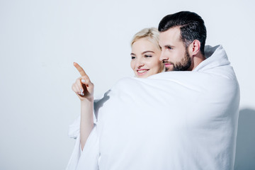 girlfriend pointing with finger near boyfriend covered in blanket on white