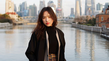 Beautiful Young Brunette Woman In Black Clothes Smiling At Camera With  Blur Shanghai Bund Landmark Buildings Background In Autumn Dusk Light. Emotions, People, Beauty, Travel And Lifestyle Concept.