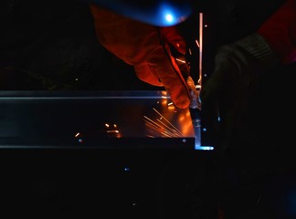 A Indian woman wearing a pink long sleeve jacket, safety welding mask and leather gloves, welding a metal case for computer server rack, with sparks