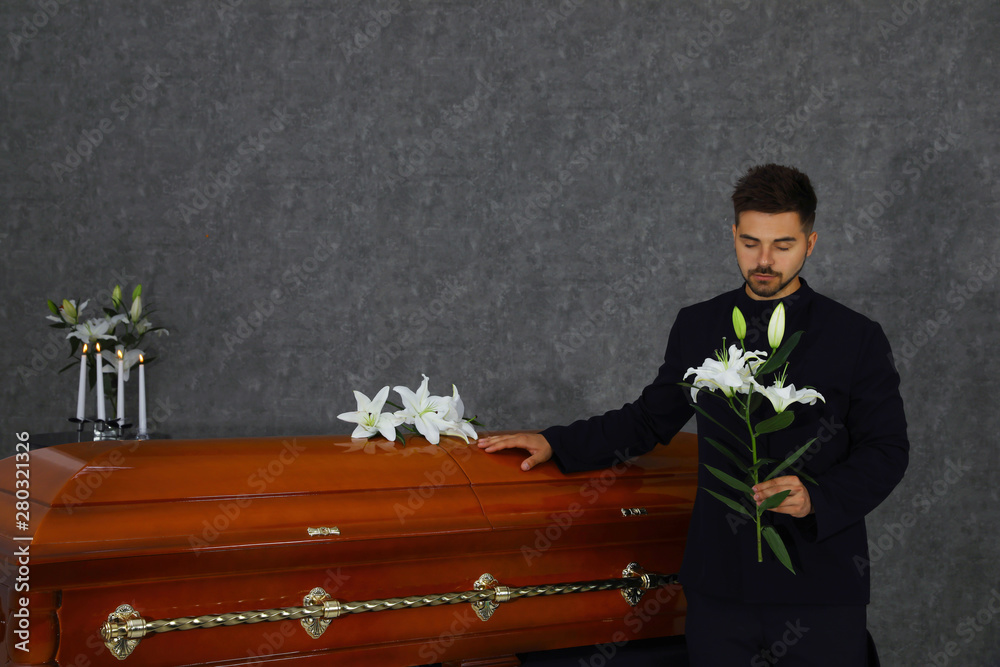 Sad young man with white lilies near casket in funeral home Stock Photo