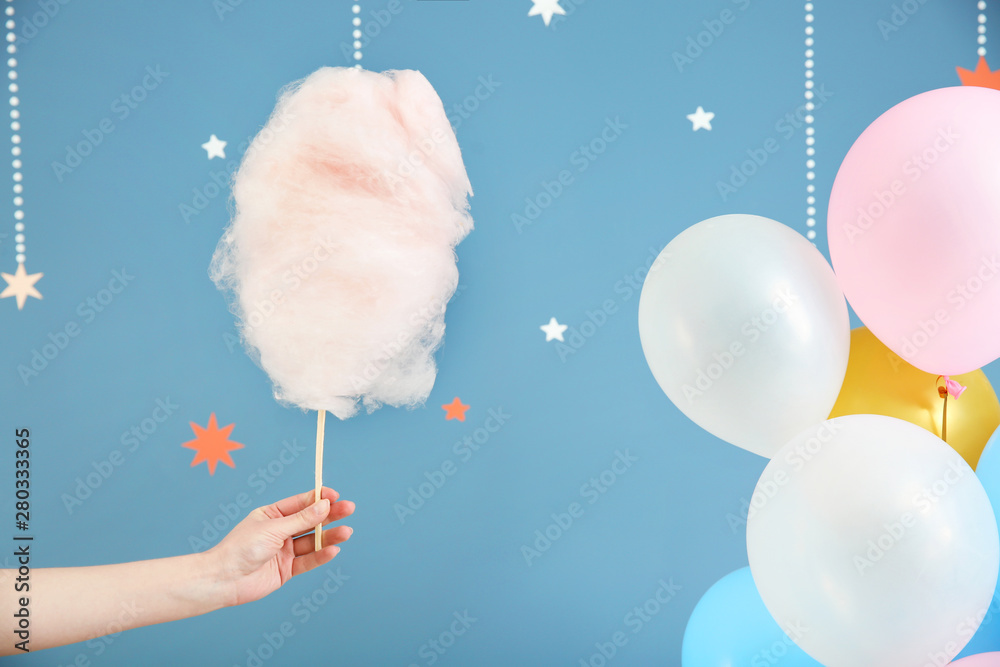 Female hand with tasty cotton candy on color background