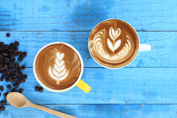 Two cups of latte art with pattern the leaves and coffee beans on blue wooden background