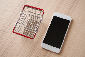 Wall Mural - Mobile phone with basket on wood table background shopping online concept