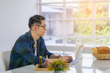Young Asian businessman working remotely from a home office with a laptop while sitting at the table