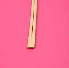 two wooden chopsticks on a pink background