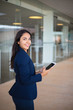 © Mangostar - Positive joyful manager using tablet in office hall. Young Latin business woman holding tablet and smiling at camera. Wireless connection concept