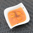 Two hungry flies on a white bowl that is filled with a tasty homemade apricot puree. The flies are on the edge of the bowl. Around the white dishware there is a dark grey rattan table. 