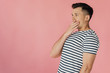 © LIGHTFIELD STUDIOS - shocked young man in striped t-shirt covering mouth with hand isolated on pink