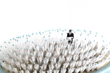 miniature person lost in a field, businessman looking at a map while standing on a hair brush