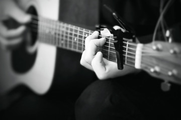 Wall Mural - Black and white image, where a person plays a melody on an acoustic six-string guitar, on the fretboard of which the strings are clamped with a capo.