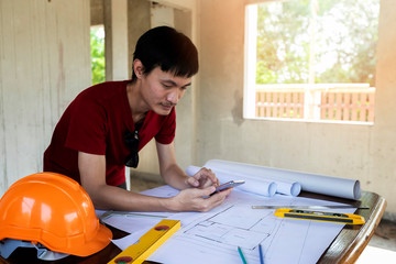 Engineer or Architect using cell phone on blueprint in building construction site.