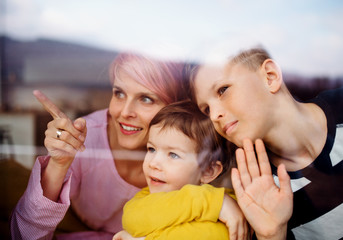 A portrait of young woman with two children at home, looking out of window.