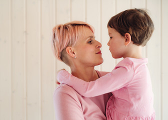 Wall Mural - A young woman with small daughter, white wooden wall in the background.