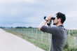 © Andreshkova Nastya - Portrait of young adventure man travelling with binoculars, watching landscape view outdoors. Young brunette man discover nature scenes. Travelling, discovering, vacation concept