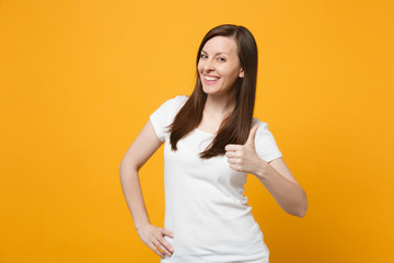 Wall Mural - Portrait of smiling successful young woman in white casual clothes looking camera, showing thumb up isolated on bright yellow orange background in studio. People lifestyle concept. Mock up copy space.