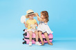 Happy kids sitting on colorful pink suitcase prepared for summer vacation. Young travelers. Little girl and boy, sister and brother, having fun isolated on blue background