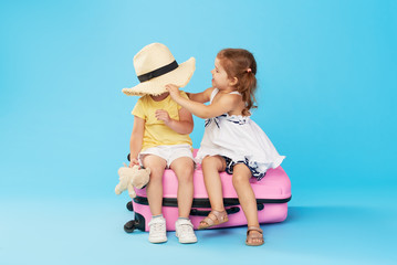 Wall Mural - Happy kids sitting on colorful pink suitcase prepared for summer vacation. Young travelers. Little girl and boy, sister and brother, having fun isolated on blue background