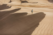 Man Walks Along Ridge Of Giant Windy Sand Dunes In Colorado