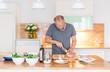 Mann steht mit dem Messer in der Küche, beweist sich als Hobbykoch und bereitet das Essen vor, Süsskartoffel, Fisch Filet, Möhren, grüner Salat, Knoblauch