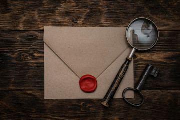 Wall Mural - old envelope with a sealing wax stamp, rusty key and a magnifying glass on a brown wooden table back