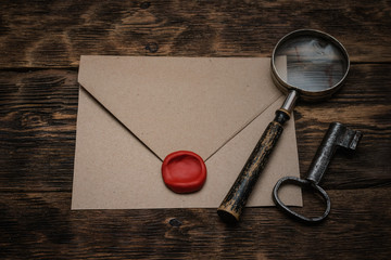 Wall Mural - old envelope with a sealing wax stamp, rusty key and a magnifying glass on a brown wooden table back