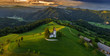 Skofja Loka, Slovenia - Aerial panoramic view of the beautiful hilltop church of Sveti Tomaz (Saint Thomas) with amazing golden sunset and the Julian Alps at background at summer time