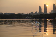 Hubble Bubbles Above Lake Ripples. Bright Sunset In Urban Skyline. Blur Buildings Background. In Century Park Shanghai China.
