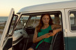 © Wavebreak Media - Beautiful woman using mobile phone on front seat of camper van at beach