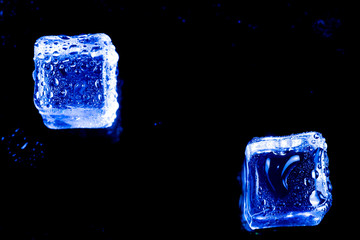 Blue ice cubes on black wet table.