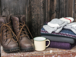 A horizontal photo of boots, scarfs and atin cup.