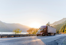 Big Rig Burgundy Semi Truck Transporting Commercial Cargo In Refrigerator Semi Trailer Driving On The Road Along Columbia River With Sunshine