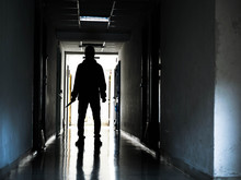 Man Silhouette Walking Away With Knife In The Light Of Opening Door In Dark Room, Threat Concept.