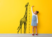 Surprised African-American Girl Measuring Height Near Color Wall With Drawn Giraffe