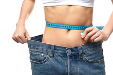 Young Woman In Loose Jeans Measuring Her Waist On White Background. Weight Loss Concept