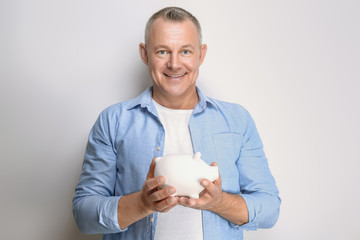 Wall Mural - Portrait of handsome middle-aged man with piggy bank on light background