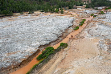 Aerial top down view; drone flying over a very polluted river with copper colored water; dumping of chemical waste into the river; dead vegetation, tree stumps; concept of environmental pollution