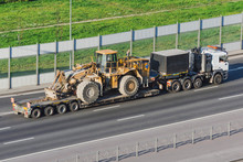 Truck With A Long Trailer Platform For Transporting Heavy Machinery, Loaded Big Tractor With Bucket. Highway Transportation.